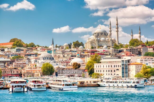 Touristic sightseeing ships in Golden Horn bay of Istanbul and view on Suleymaniye mosque with Sultanahmet district against blue sky and clouds. Istanbul, Turkey during sunny summer day.